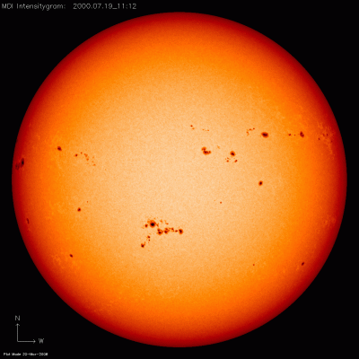 Image of the Sun with dark sunspots scattered across its surface, appearing as black dots