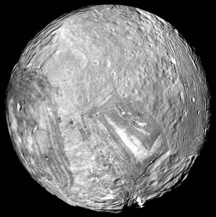 Image of Miranda, one of Uranus's moons, showing a heavily cratered and grooved surface with large faults and ridges